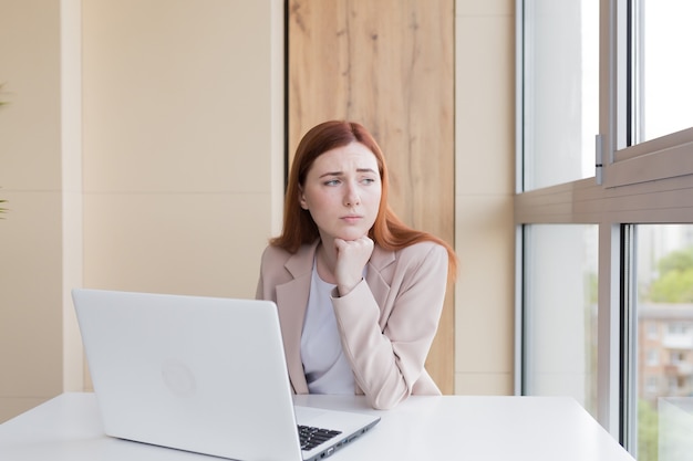 Mujer de negocios pelirroja molesta que trabaja en la computadora sentado en la oficina