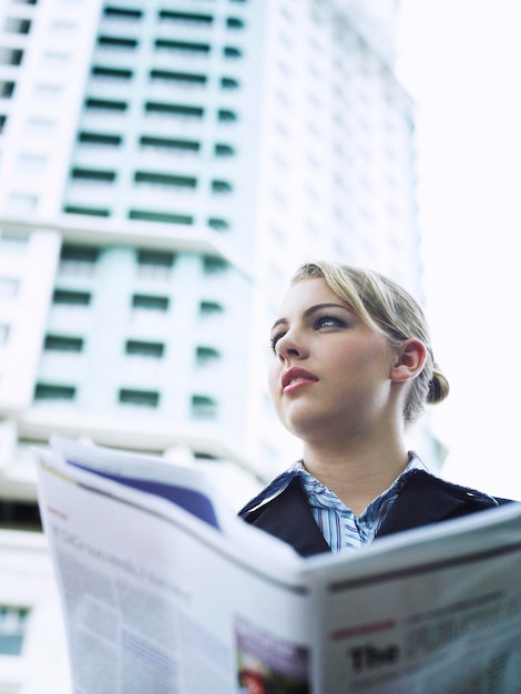 Foto mujer de negocios con un periódico de pie junto al edificio