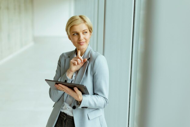 Mujer de negocios de pie con tableta digital en el pasillo de la oficina