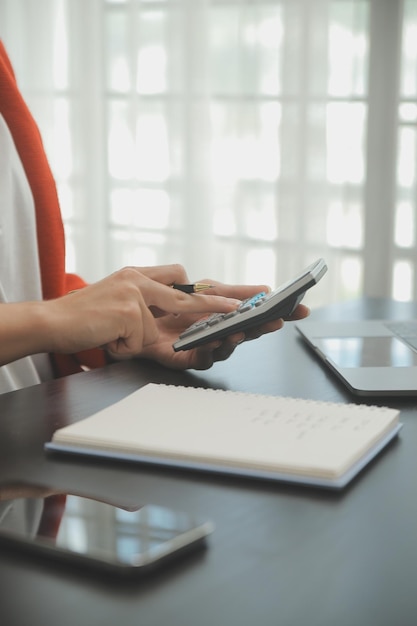 Mujer de negocios de primer plano que usa calculadora y computadora portátil para hacer finanzas matemáticas en estadísticas de contabilidad fiscal de escritorio de madera y concepto de investigación analítica