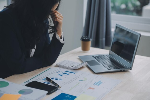 Mujer de negocios de primer plano que usa calculadora y computadora portátil para hacer finanzas matemáticas en estadísticas de contabilidad fiscal de escritorio de madera y concepto de investigación analítica