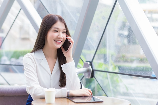 Mujer de negocios profesional asiática joven hermosa en una camisa blanca es mientras usa su teléfono inteligente