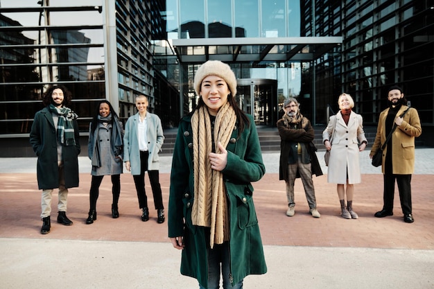 Foto mujer de negocios que se destaca de un grupo diverso de empresarios mientras posan juntos fuera del edificio de oficinas.