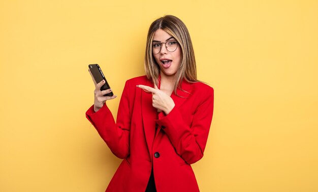 Mujer de negocios que parece emocionada y sorprendida señalando el concepto de teléfono inteligente lateral