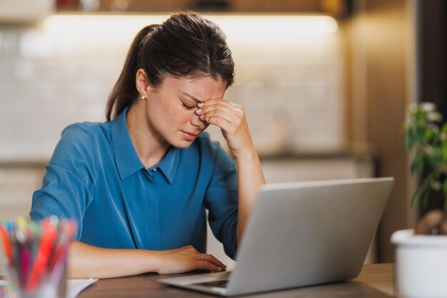 Mujer de negocios que parece preocupada mientras trabaja en la computadora portátil en casa.