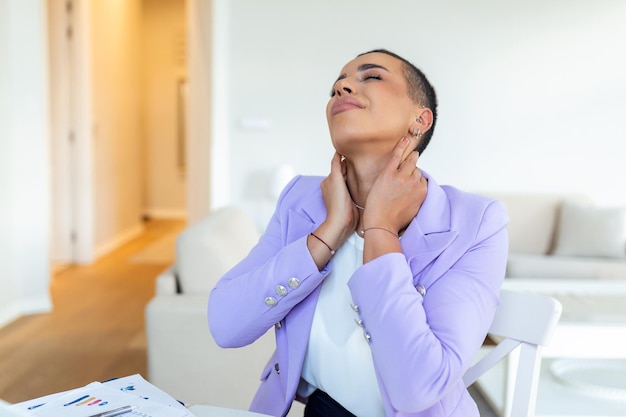 Mujer de negocios que siente dolor en el cuello después de sentarse en la mesa con una computadora portátil Mujer cansada que sufre del síndrome de la oficina debido a largas horas de trabajo en la computadora Chica bonita masajeando los músculos tensos del cuello