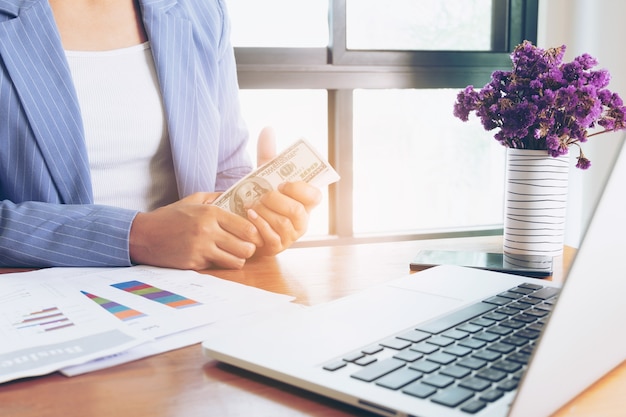 Mujer de negocios que sostiene el billete de dólar en la mano en la oficina