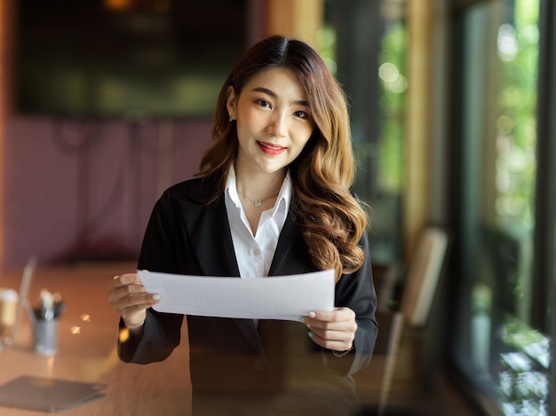 Mujer de negocios que sostiene el informe comercial de la carta de la factura del papel que se coloca en retrato de la sala de juntas de la oficina