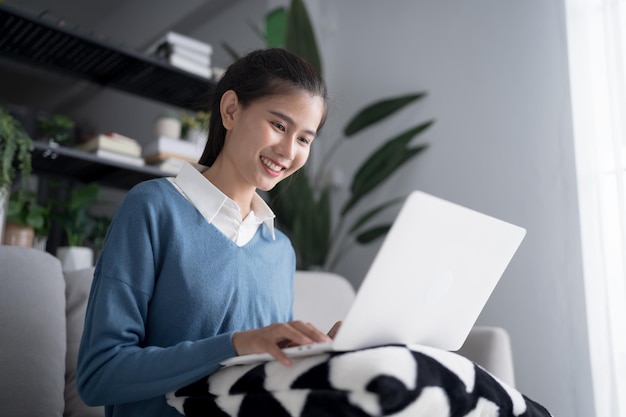 Mujer de negocios que trabaja desde casa, trabaja en línea en una computadora portátil, mujer de negocios asiática que trabaja en un sofá, negocios en línea con distanciamiento social, reunión en línea con computadora portable.