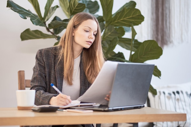 Mujer de negocios que trabaja con una computadora portátil Escribiendo algo idea en un cuaderno o en una lista de verificación en la oficina