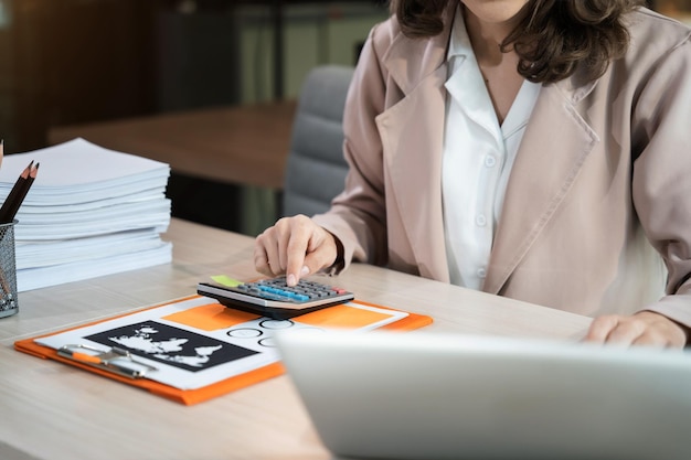 Mujer de negocios que trabaja en la oficina de escritorio usando una calculadora para calcular el concepto de contabilidad financiera de números