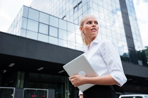 Mujer de negocios que trabaja con la tableta al aire libre de pie cerca de la oficina