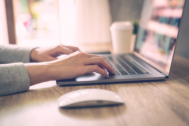 La mujer de negocios que usa la computadora portátil hace actividad en línea en la tabla de madera en la oficina en casa.