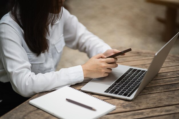 Mujer de negocios que usa un teléfono inteligente después de trabajar con una computadora portátil en la mesa mujer de negocios que usa un teléfono móvil para buscar o en las redes sociales o comprar en línea o almacenar una conferencia de conversación de teléfonos inteligentes