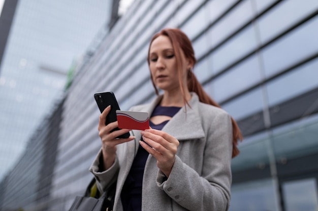 La mujer de negocios que usa un teléfono móvil en el fondo de un edificio de oficinas paga los bienes con un