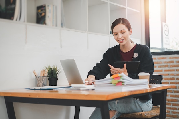 Mujer de negocios que utiliza una tableta y una computadora portátil para analizar el informe de negocios en la oficina