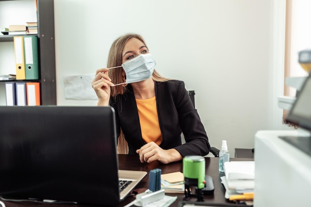 La mujer de negocios se quita la máscara médica de la cara en la oficina