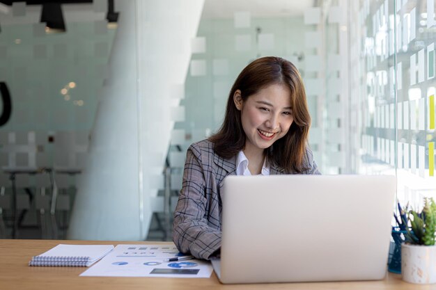 Una mujer de negocios revisa los documentos financieros de la empresa y usa una computadora portátil para hablar con el director financiero a través de un programa de mensajería. Concepto de gestión financiera de la empresa.