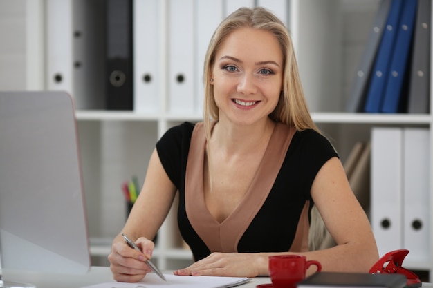 Mujer de negocios rubia en formación, toma notas en papel y mira a cámara.