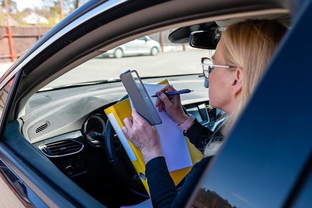 Mujer de negocios rubia de mediana edad con gafas en un automóvil que trabaja con documentos concepto de tecnología móvil