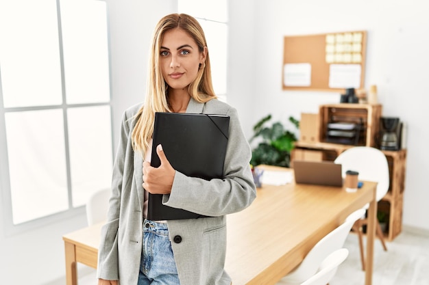 Mujer de negocios rubia en la oficina relajada con expresión seria en la cara simple y natural mirando a la cámara