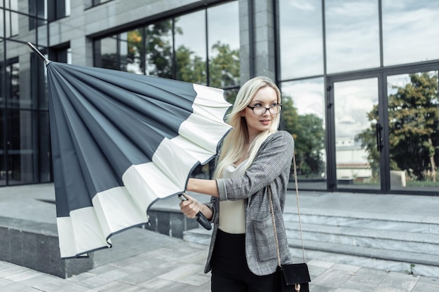 Mujer de negocios rubia paraguas abierto en el fondo de una oficina de negocios. esperando la lluvia