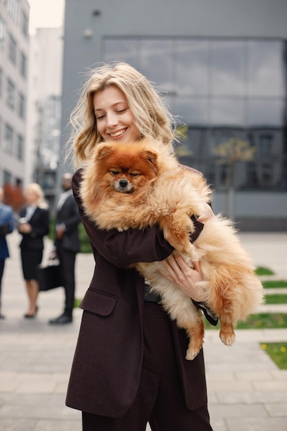 Mujer de negocios rubia de pie y sosteniendo un perro frente a la oficina moderna