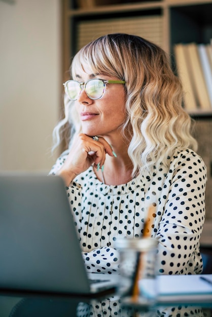 Mujer de negocios rubia que trabaja gratis en la oficina mirando afuera y pensando con una sonrisa Empresaria feliz mujer con gafas Descanso del concepto de actividad laboral Trabajador en línea moderno