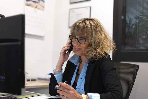 Mujer de negocios rubia trabajando en la oficina y hablando por teléfono
