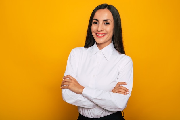 Mujer de negocios segura exitosa feliz moderna en una camisa blanca está planteando sobre fondo amarillo