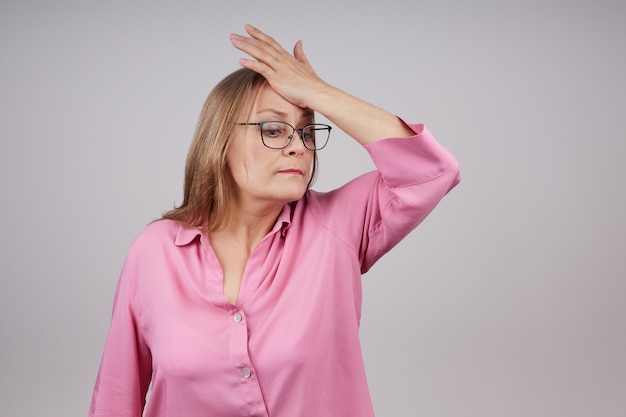 Mujer de negocios senior con gafas tiene dolor de cabeza. Foto de estudio sobre un fondo gris, con espacio de copia.