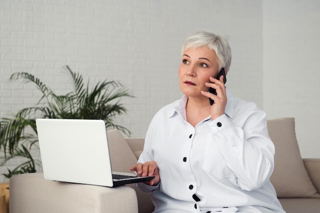 Mujer de negocios senior o profesional independiente que trabaja con un teléfono inteligente y una computadora portátil