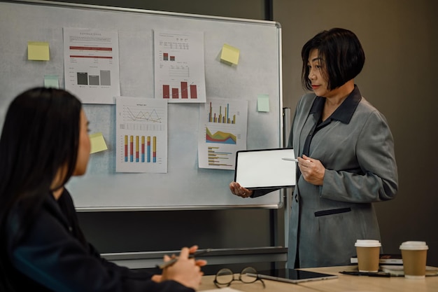 Mujer de negocios sénior segura sosteniendo una tableta digital y explicando la investigación de datos a su equipo