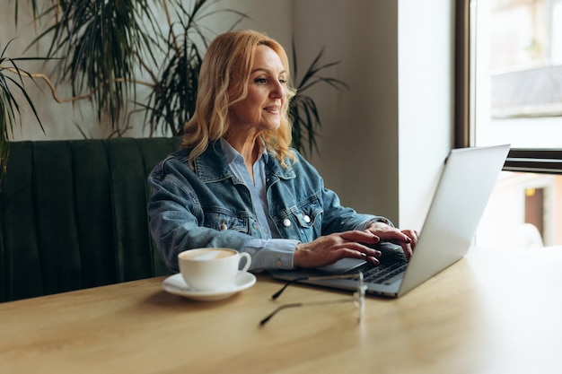 Mujer de negocios senior sentada en una cafetería y trabajando en una computadora portátil Mujer madura en un café usando una computadora portátil