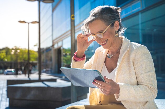 Mujer de negocios senior con tecnología feliz trabajando con una tableta en una ciudad moderna