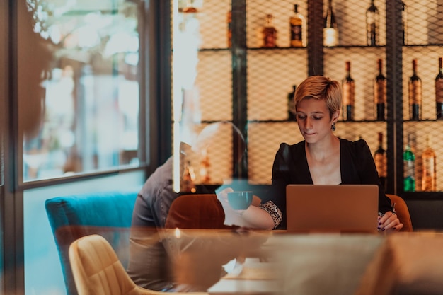 Mujer de negocios sentada en un café mientras se centra en trabajar en una computadora portátil y participa en una reunión en línea Foco selectivo Foto de alta calidad