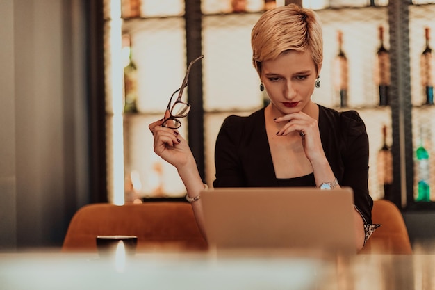 Mujer de negocios sentada en un café mientras se centra en trabajar en una computadora portátil y participa en una reunión en línea Foco selectivo Foto de alta calidad