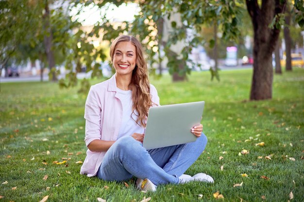 Mujer de negocios sentada en el parque de verano de hierba usando una computadora portátil Persona de negocios que trabaja a distancia al aire libre