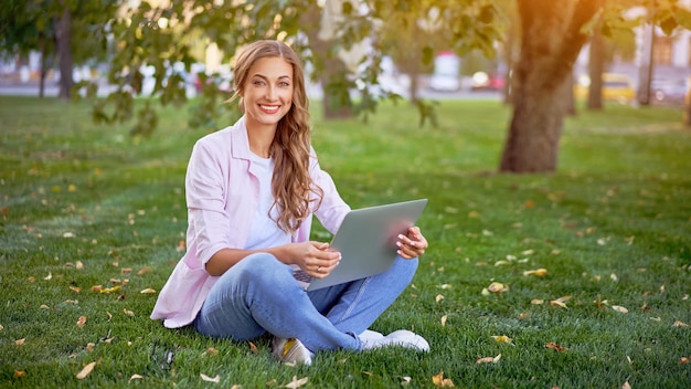 Mujer de negocios sentada en el parque de verano de hierba usando una computadora portátil Persona de negocios que trabaja a distancia al aire libre