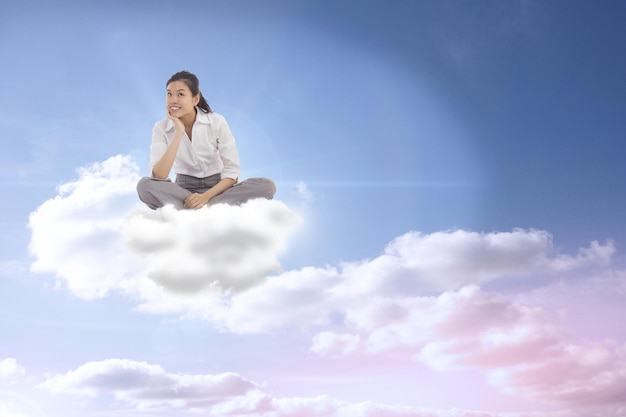 Mujer de negocios sentada con las piernas cruzadas pensando contra el hermoso cielo azul nublado