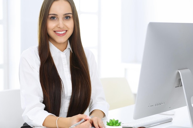 Mujer de negocios sentada y trabajando con la computadora en la oficina blanca