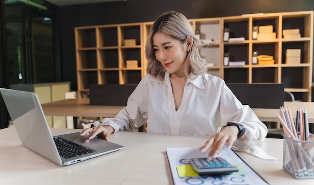 Mujer de negocios sentada trabajando en una computadora portátil y usando una máquina calculadora análisis documento ingresos trabajo factura factura banco