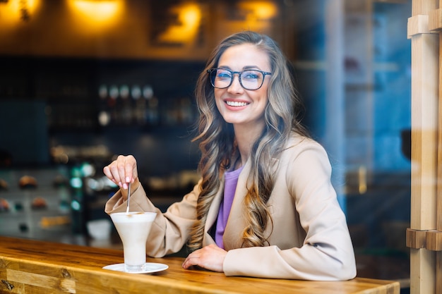 Mujer de negocios sentado café detrás de la ventana esperando socio de negocios mujer caucásica descansando cafetería beber café tardío sonrisa mirando afuera