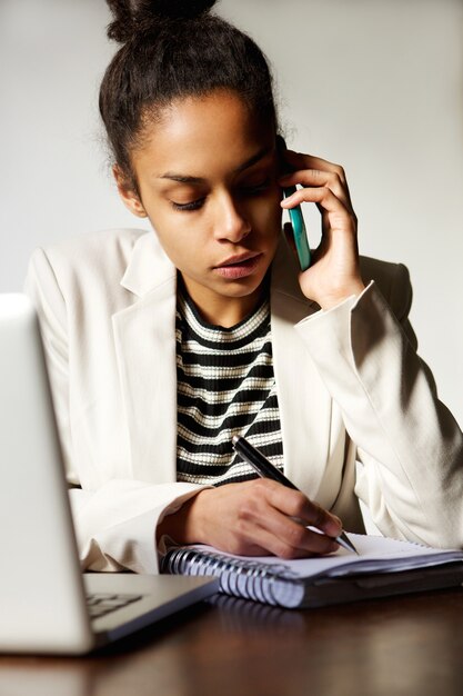 Mujer de negocios sentado en el escritorio hablando por teléfono móvil