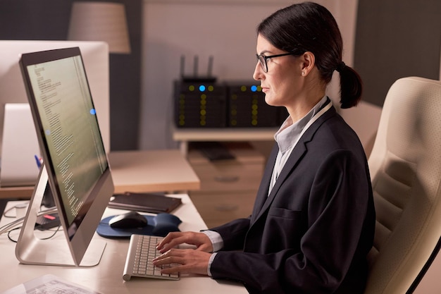 Mujer de negocios seria que usa computadora mientras trabaja de noche en la oficina de TI