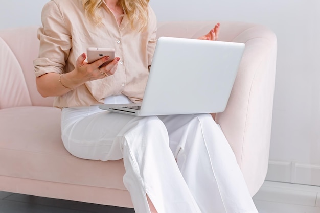 Una mujer de negocios se sienta con una computadora portátil gris abierta de rodillas y sostiene un teléfono inteligente rosa