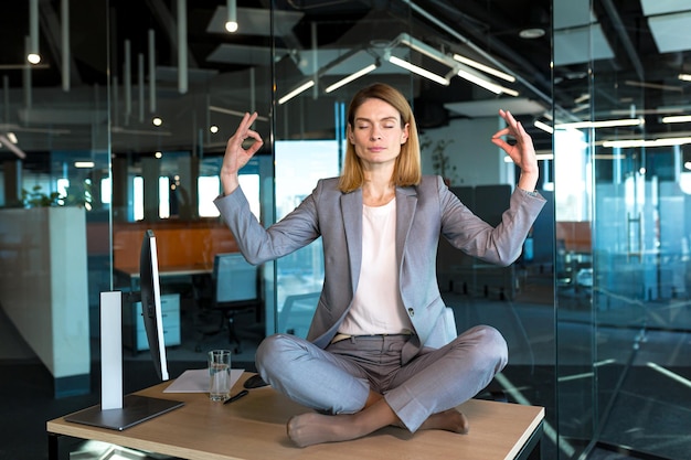 Mujer de negocios sola sentada en el escritorio en su oficina empleada meditando en posición de loto
