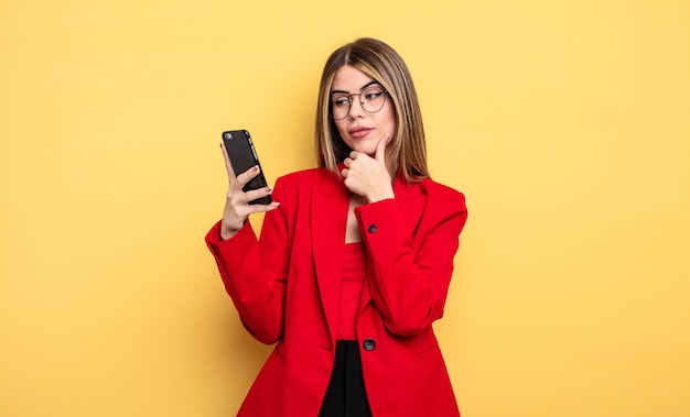 Mujer de negocios sonriendo con una expresión feliz y segura con la mano en la barbilla. concepto de teléfono inteligente