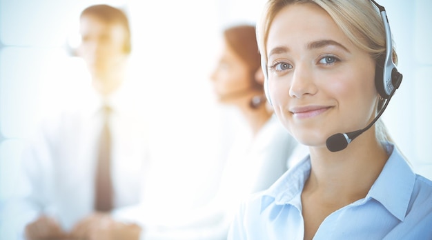 Mujer de negocios sonriente alegre con auriculares consultando a clientes. Grupo de diversos operadores telefónicos en el trabajo en la oficina soleada. Centro de llamadas y concepto de gente de negocios.