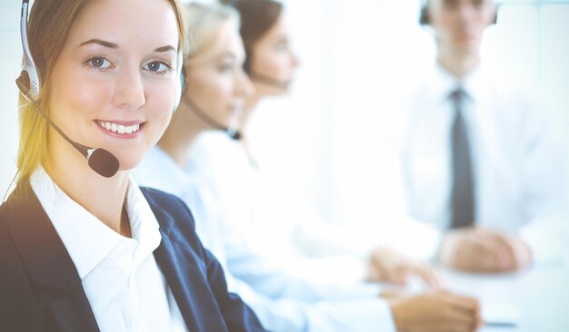 Mujer de negocios sonriente alegre con auriculares consultando a clientes. Grupo de diversos operadores telefónicos en el trabajo en la oficina soleada. Centro de llamadas y concepto de gente de negocios.